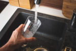 Filling glass of water from stainless steel kitchen faucet. Drinking water concept