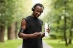 Happy black guy using phone and drinking water, training outdoors