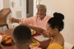 Happy  African American grand father sitting at the dinning table and raising his glass of water for toasting with his family at home