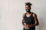 Image of african american sportsman smiling and posing with water bottle