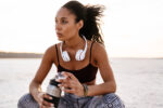 Image of young african american sportswoman squatting with water bottle