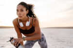 Image of young african american sportswoman standing with water bottle