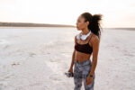 Image of young african american sportswoman standing with water bottle