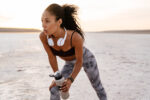 Image of young african american sportswoman standing with water bottle