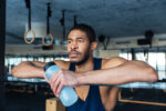 Pensive sports man holding bottle with water in the gym