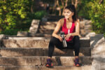 Smiling young sportswoman sitting on stairs with water bottle