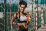 Woman in sportswear with wireless headphones and fitness tracker holding bottle of water