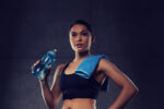 woman with towel drinking water from bottle in gym