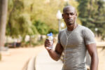 Young black man drinking water before running in urban backgroun