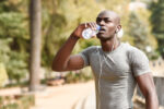 Young black man drinking water before running in urban backgroun