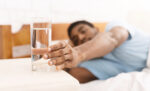 Young man taking glass of water in bed