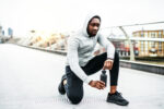 Young sporty black man runner with water bottle on the bridge in a city, resting.